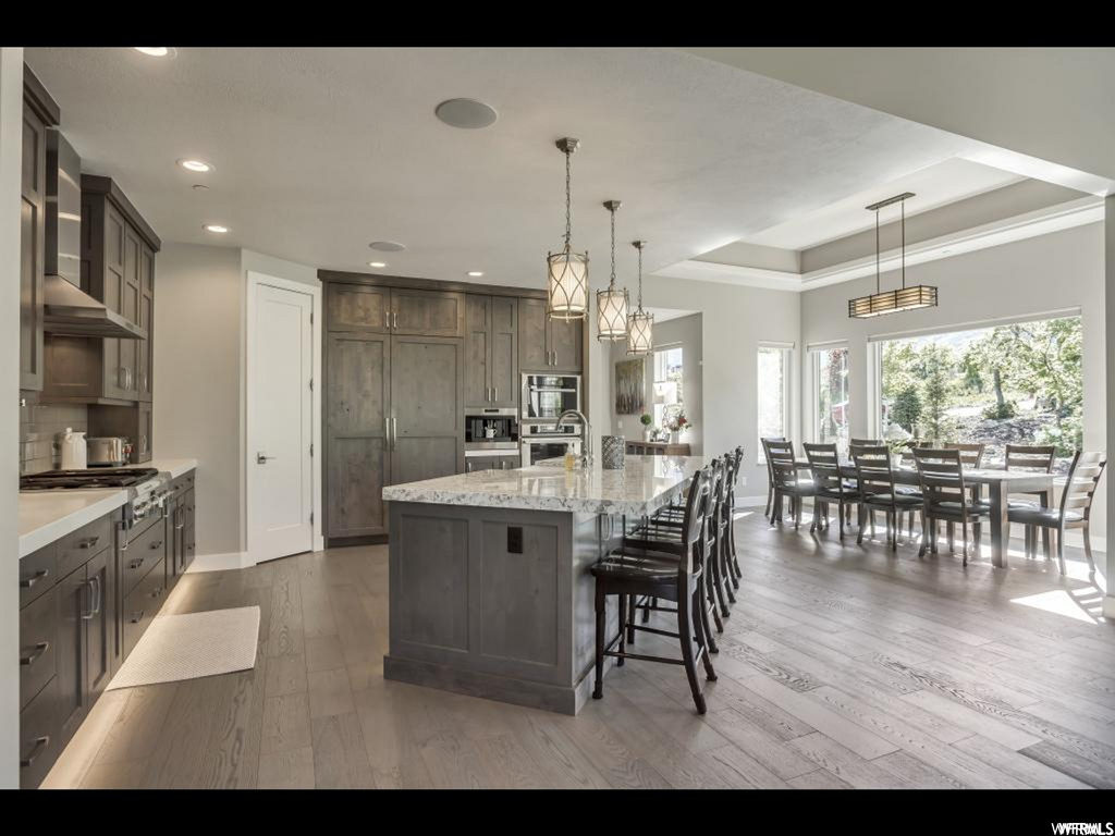 Kitchen with hanging light fixtures, a kitchen island with sink, a raised ceiling, and light hardwood / wood-style flooring