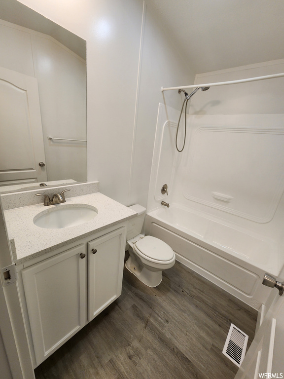 Full bathroom with bathing tub / shower combination, toilet, hardwood / wood-style floors, and vanity with extensive cabinet space