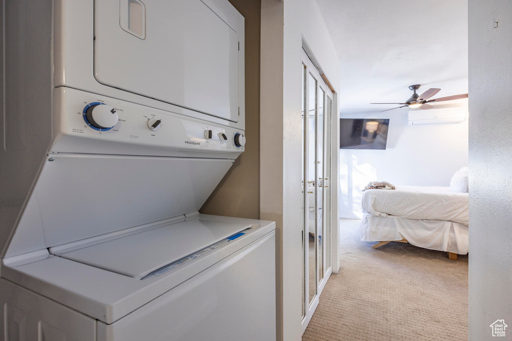 Laundry area featuring a wall unit AC, stacked washer / dryer, light colored carpet, and ceiling fan