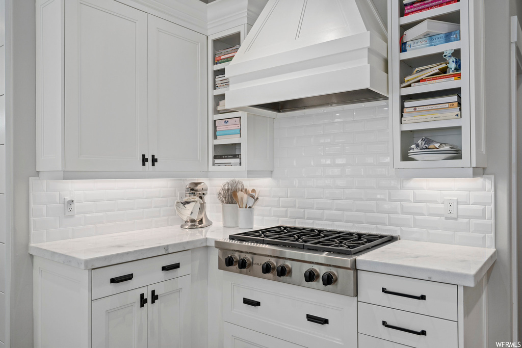 Kitchen with stainless steel gas cooktop, custom exhaust hood, white cabinets, and backsplash
