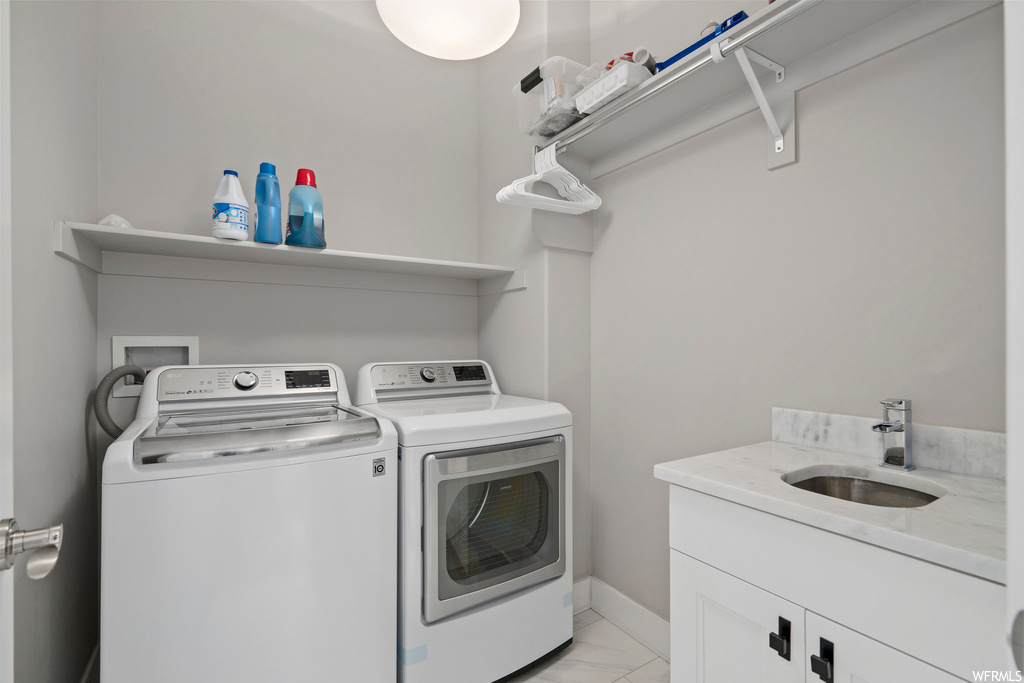 Clothes washing area featuring light tile flooring, sink, washing machine and dryer, and cabinets