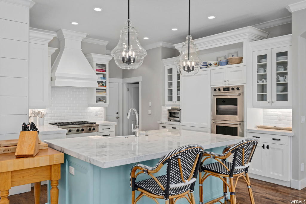 Kitchen with pendant lighting, custom exhaust hood, tasteful backsplash, stainless steel double oven, and white cabinetry