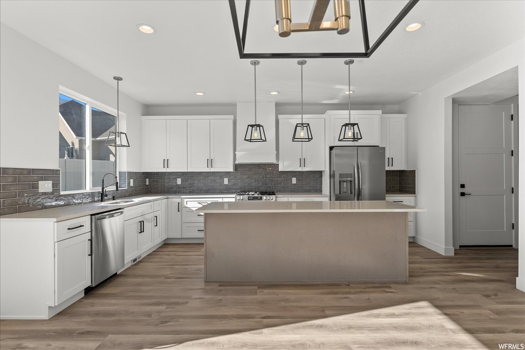 Kitchen with a center island, light wood-type flooring, appliances with stainless steel finishes, and decorative light fixtures
