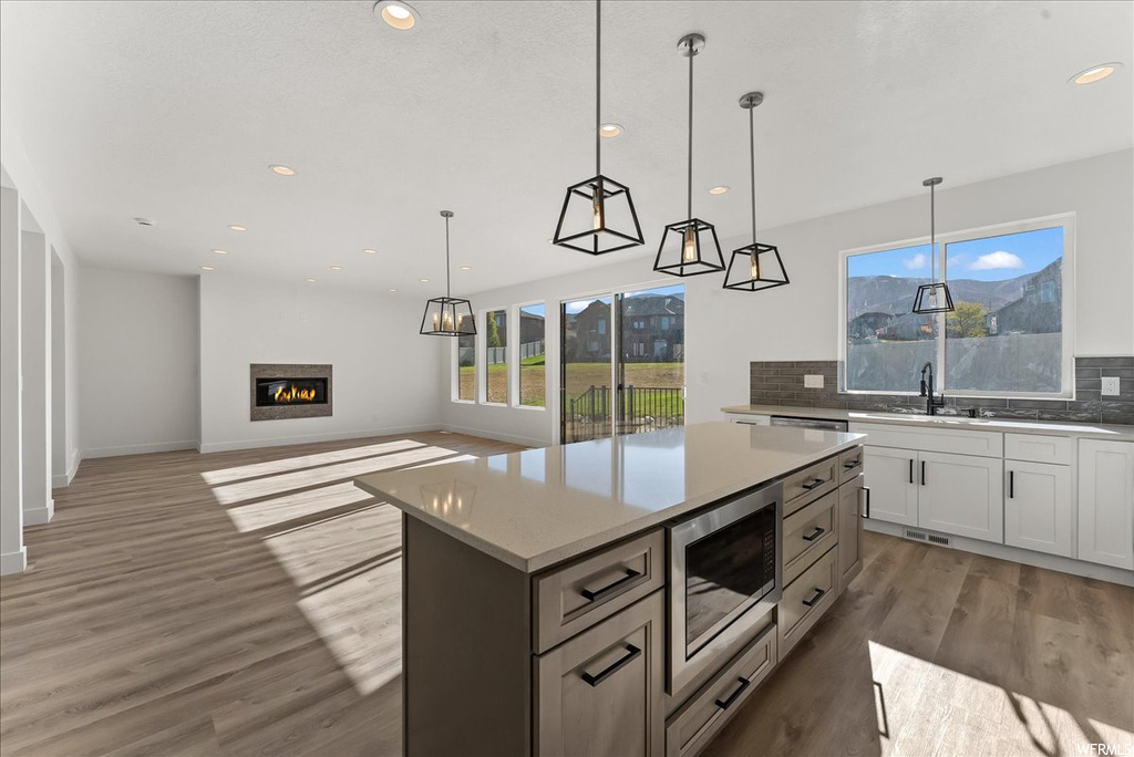 Kitchen featuring decorative light fixtures, a kitchen island, tasteful backsplash, and stainless steel microwave