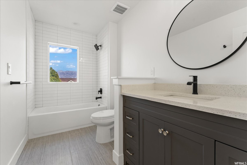 Full bathroom featuring toilet, tile flooring, tiled shower / bath, and vanity with extensive cabinet space