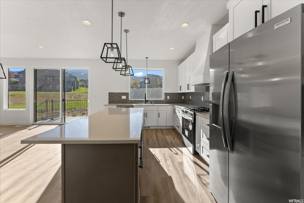 Kitchen with a center island, appliances with stainless steel finishes, pendant lighting, light hardwood / wood-style floors, and white cabinetry