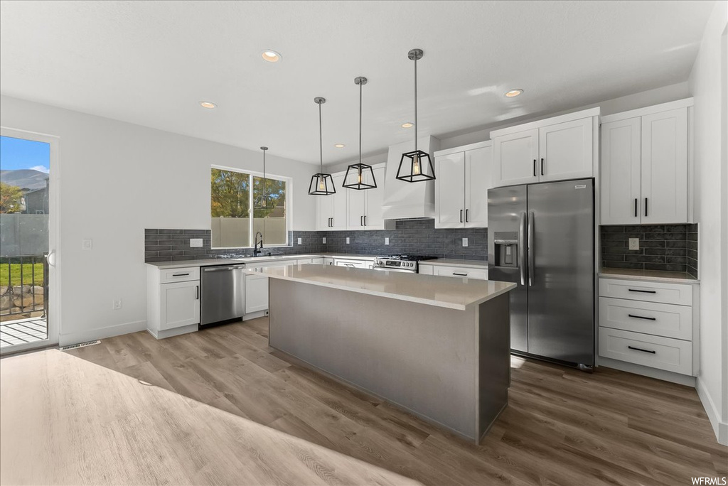 Kitchen with light hardwood / wood-style floors, pendant lighting, appliances with stainless steel finishes, white cabinets, and a kitchen island