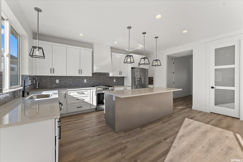 Kitchen with premium range hood, hanging light fixtures, hardwood / wood-style floors, a center island, and stainless steel appliances