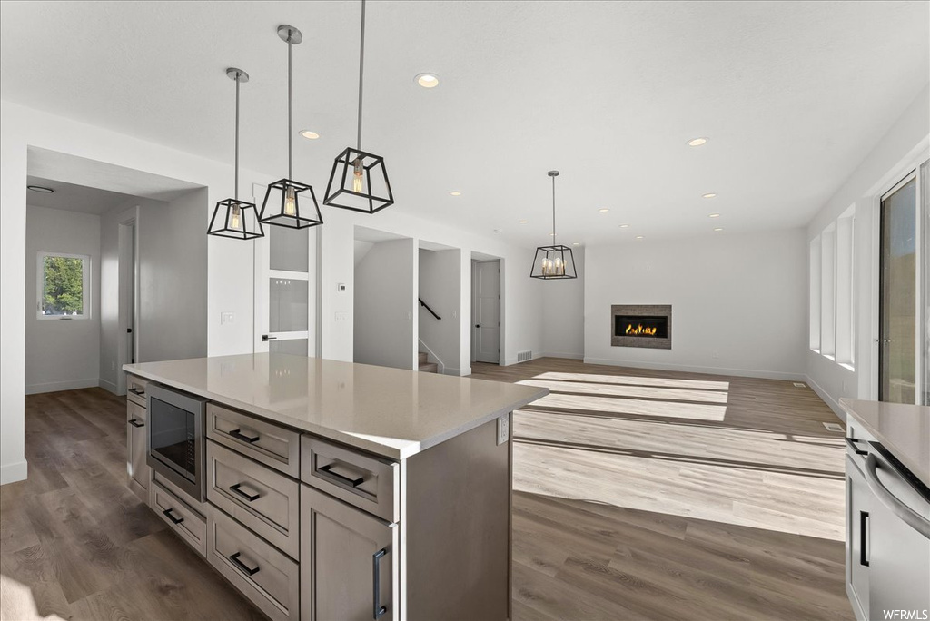 Kitchen featuring stainless steel microwave, dark wood-type flooring, a kitchen island, gray cabinets, and decorative light fixtures