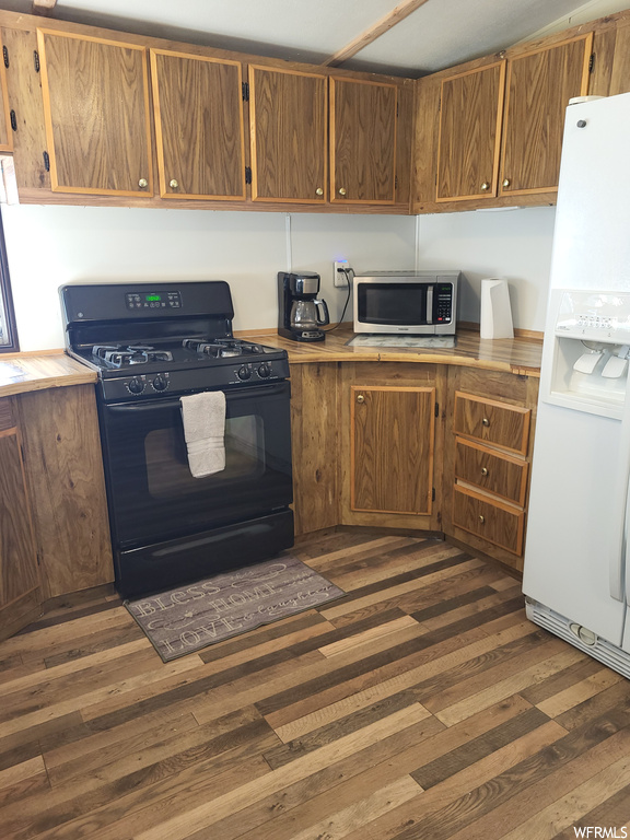 Kitchen with dark wood-type flooring, white refrigerator with ice dispenser, and black gas stove