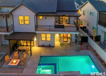 Rear view of property with a swimming pool with hot tub, a patio, a balcony, and a fire pit
