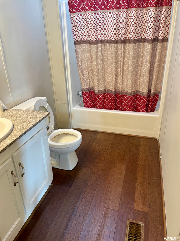 Full bathroom with hardwood / wood-style floors, toilet, vanity, and shower / bath combo with shower curtain