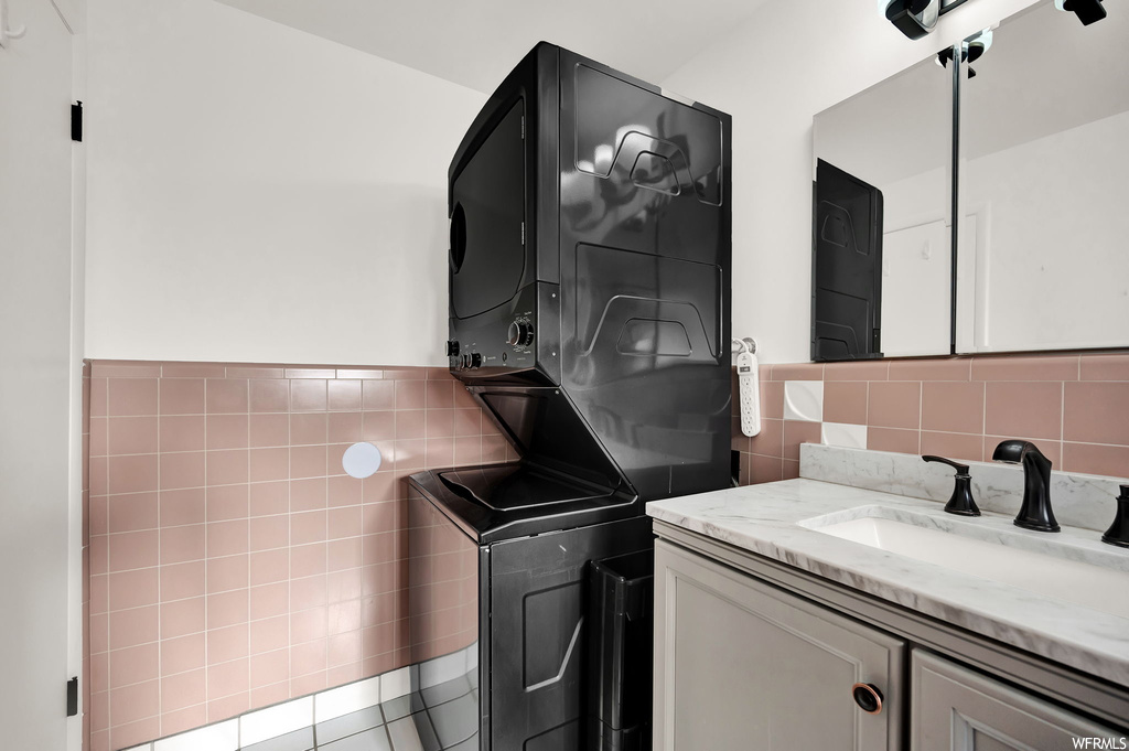 Laundry room featuring sink, tile floors, tile walls, and stacked washer / drying machine