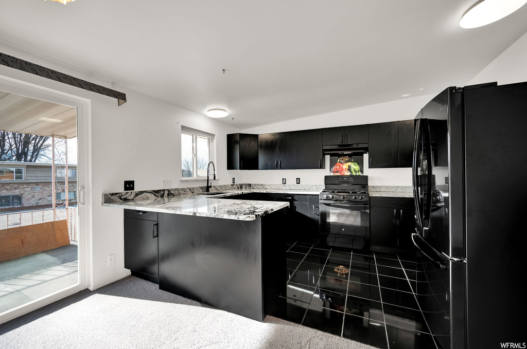 Kitchen featuring kitchen peninsula, gas range oven, sink, and black refrigerator