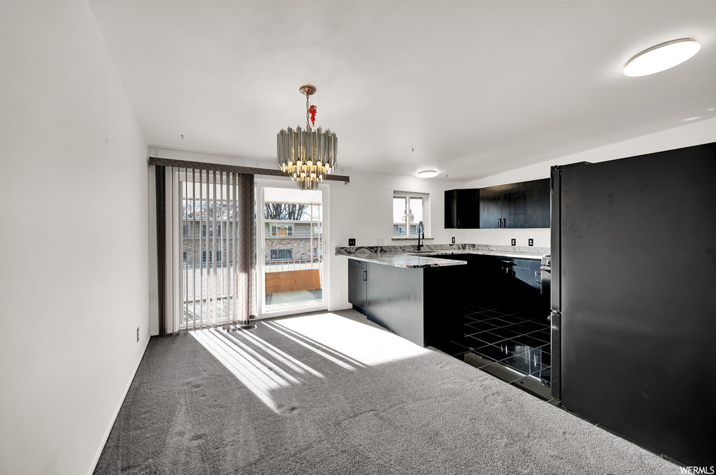 Kitchen featuring dark carpet, a notable chandelier, hanging light fixtures, and black refrigerator