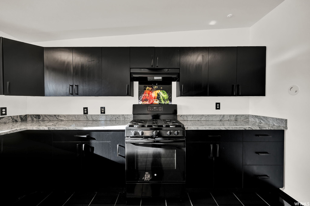 Kitchen with lofted ceiling, black gas range, and light stone counters