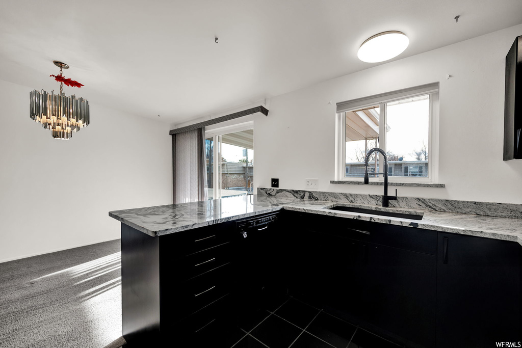 Kitchen with dark tile flooring, sink, light stone countertops, and decorative light fixtures