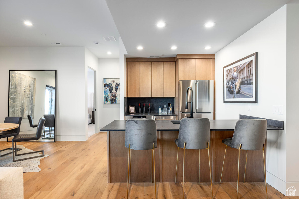Kitchen featuring a center island, a breakfast bar, light wood-type flooring, refrigerator, and backsplash