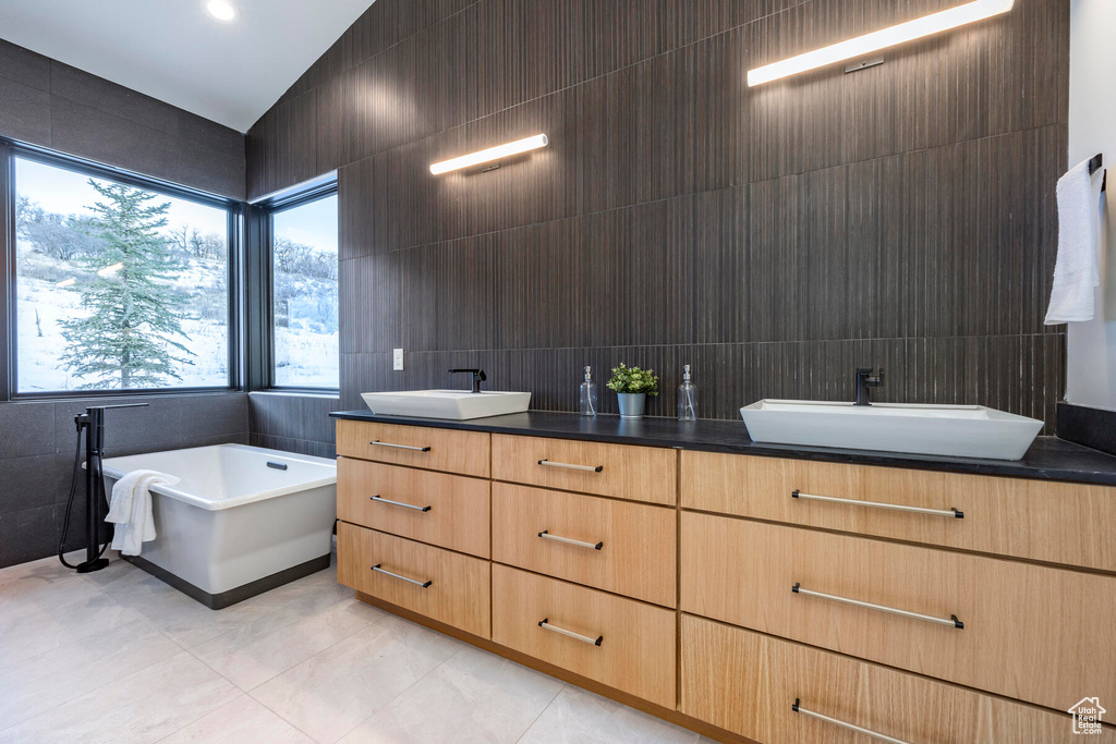 Bathroom featuring tile walls, dual bowl vanity, a bath, and tile flooring
