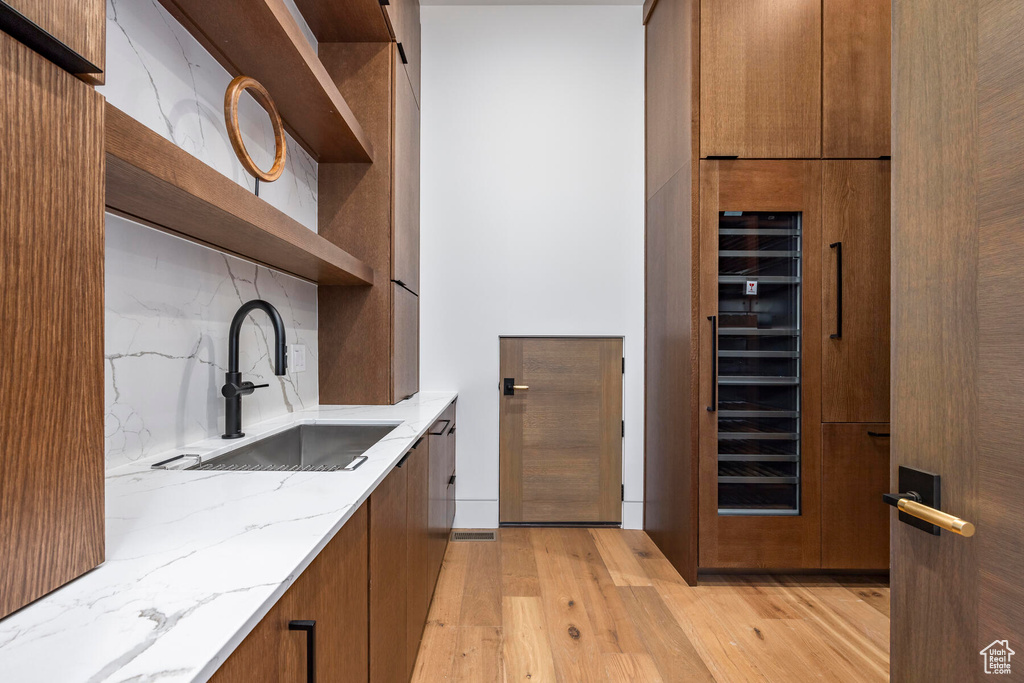 Kitchen featuring light stone countertops, backsplash, wine cooler, sink, and light wood-type flooring
