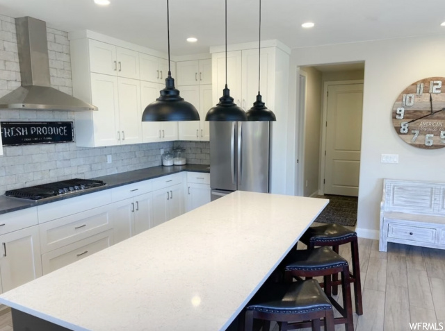 Kitchen featuring wall chimney range hood, stainless steel appliances, pendant lighting, and tasteful backsplash