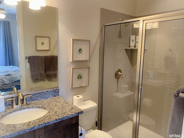 Bathroom featuring toilet, ceiling fan, a shower with shower door, and vanity