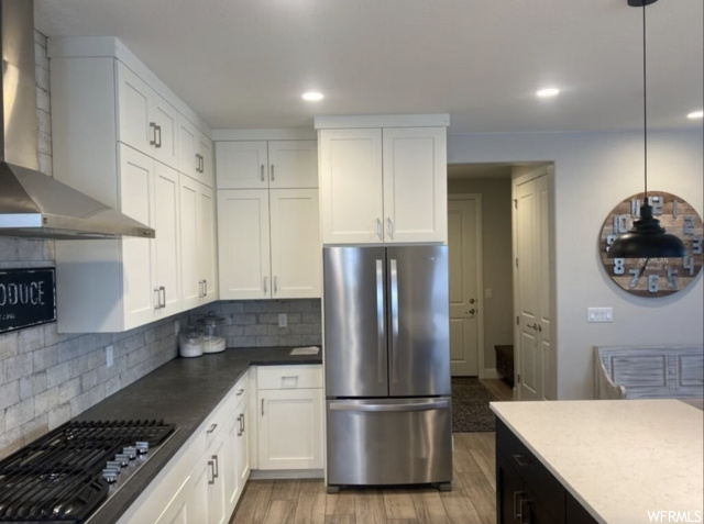 Kitchen featuring pendant lighting, white cabinetry, stainless steel appliances, and wall chimney range hood
