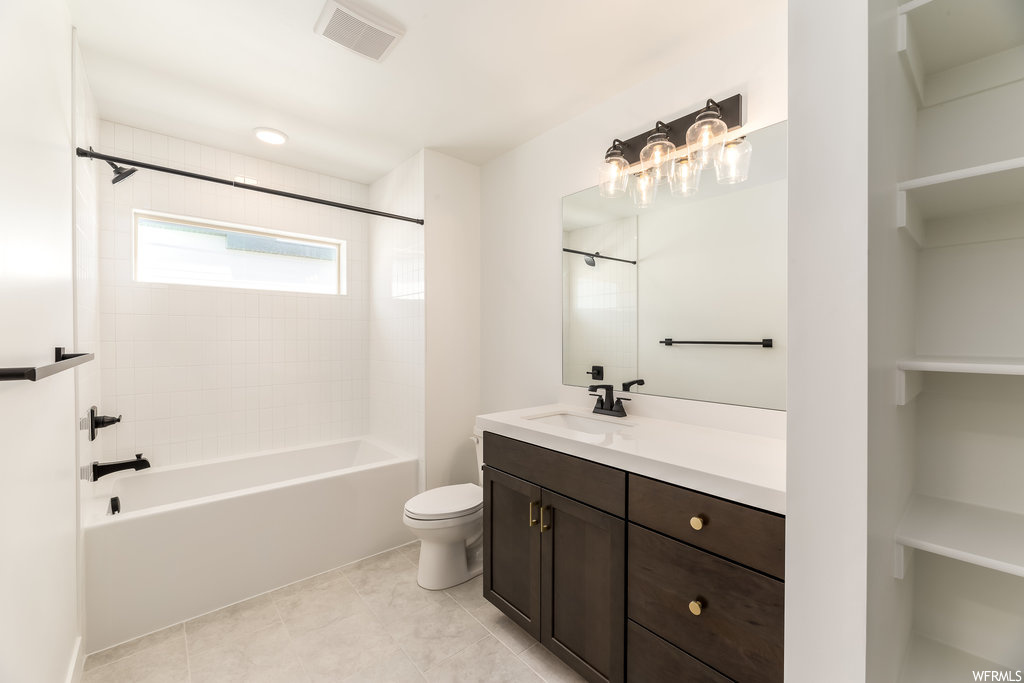 Full bathroom with tiled shower / bath combo, toilet, tile flooring, and vanity