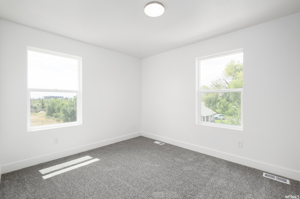Unfurnished room featuring dark carpet and plenty of natural light