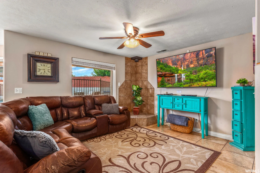 Tiled living room with ceiling fan, a textured ceiling, and tile walls