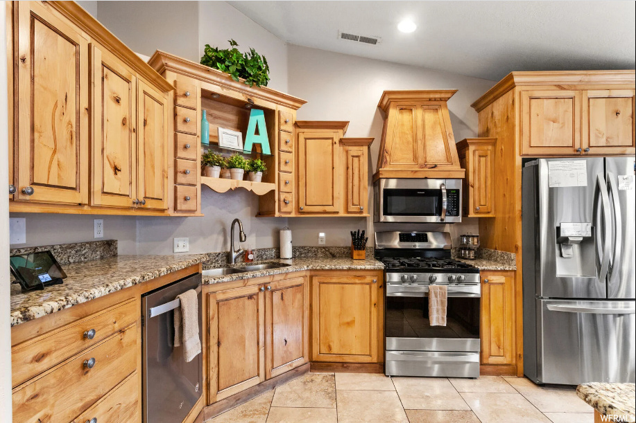 Kitchen featuring sink, light stone counters, vaulted ceiling, light tile flooring, and stainless steel appliances
