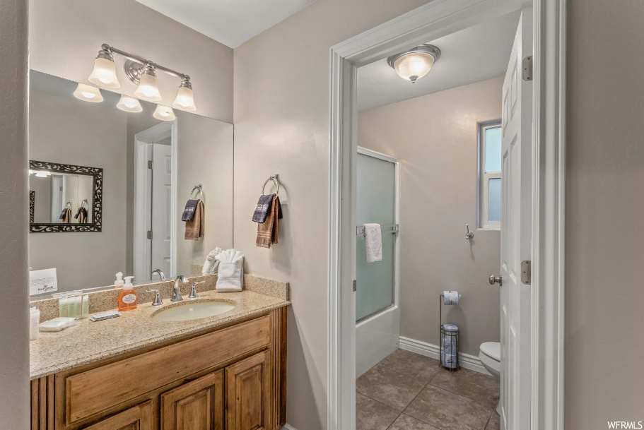 Full bathroom featuring toilet, tile floors, combined bath / shower with glass door, and vanity