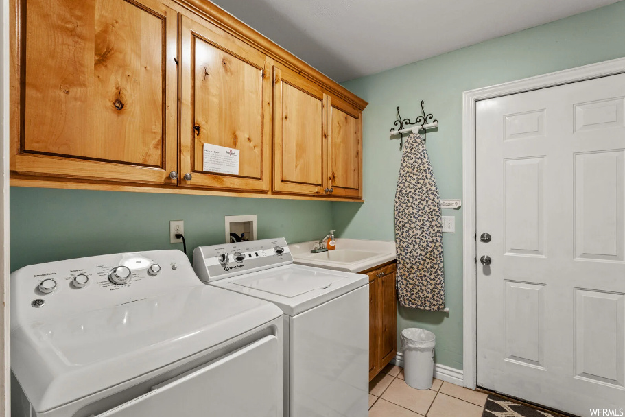Clothes washing area with independent washer and dryer, light tile floors, sink, washer hookup, and cabinets