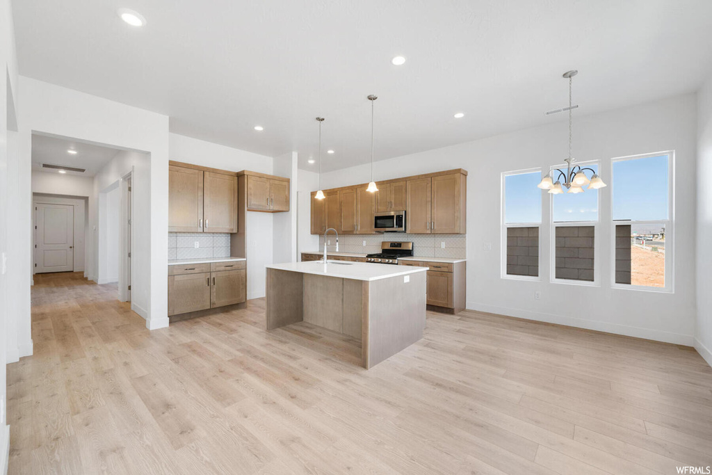 Kitchen featuring backsplash, light hardwood / wood-style floors, decorative light fixtures, and appliances with stainless steel finishes