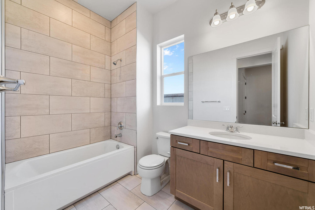 Full bathroom with tiled shower / bath combo, toilet, tile floors, and vanity