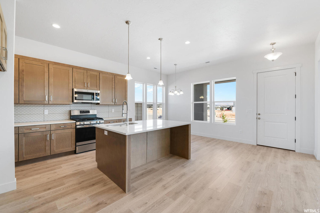 Kitchen featuring sink, appliances with stainless steel finishes, light hardwood / wood-style floors, an island with sink, and decorative light fixtures