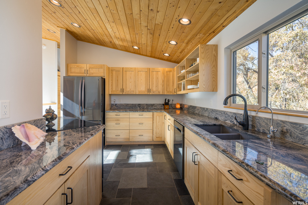 Kitchen with lofted ceiling, stainless steel refrigerator, dark stone countertops, and light brown cabinets