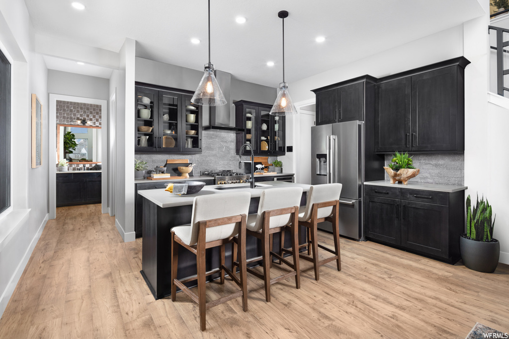 Kitchen featuring pendant lighting, light wood-type flooring, a kitchen island with sink, and tasteful backsplash