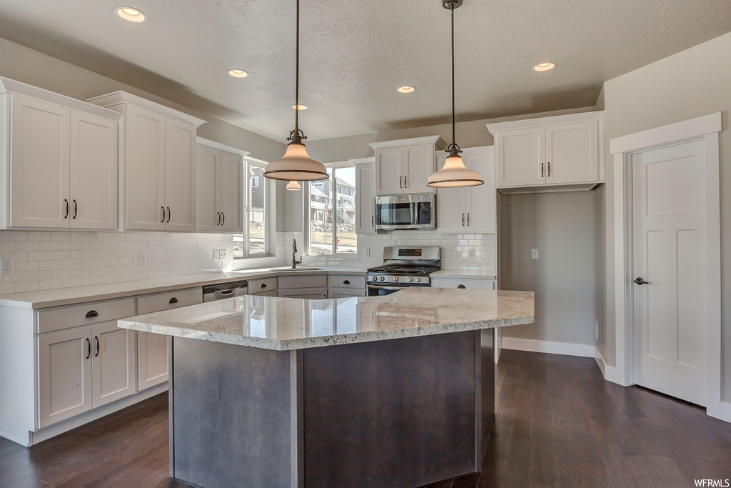 Kitchen featuring dark hardwood / wood-style floors, appliances with stainless steel finishes, decorative light fixtures, and white cabinetry
