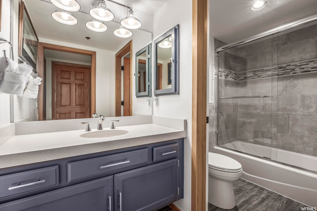 Full bathroom with toilet, vanity, hardwood / wood-style flooring, and shower / bath combination with glass door