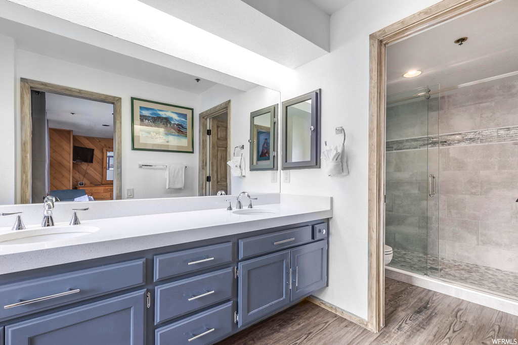 Bathroom featuring toilet, double sink vanity, a shower with door, and wood-type flooring