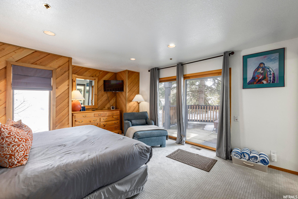 Carpeted bedroom featuring access to exterior, wood walls, and multiple windows