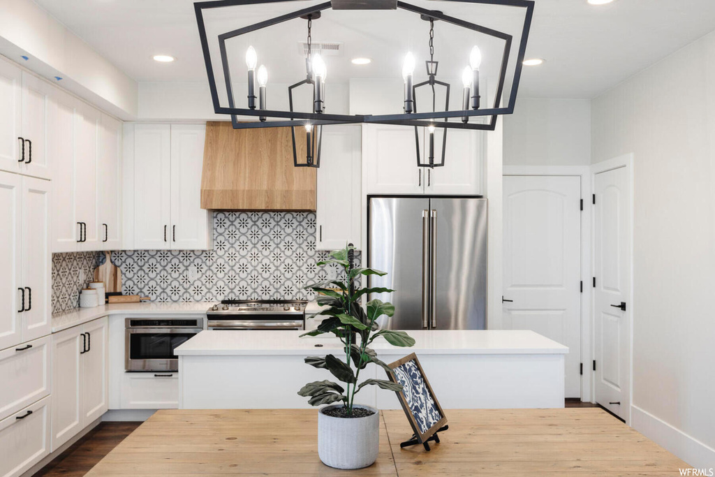Kitchen featuring dark hardwood / wood-style flooring, custom range hood, a chandelier, appliances with stainless steel finishes, and white cabinetry