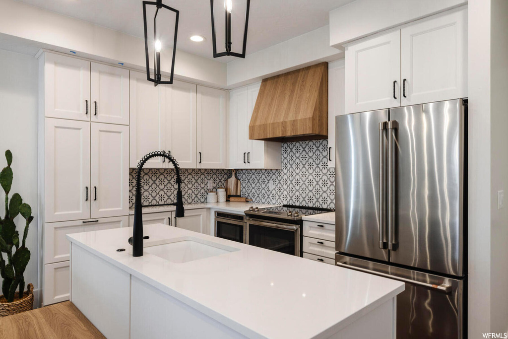 Kitchen featuring sink, stainless steel appliances, custom exhaust hood, white cabinets, and tasteful backsplash