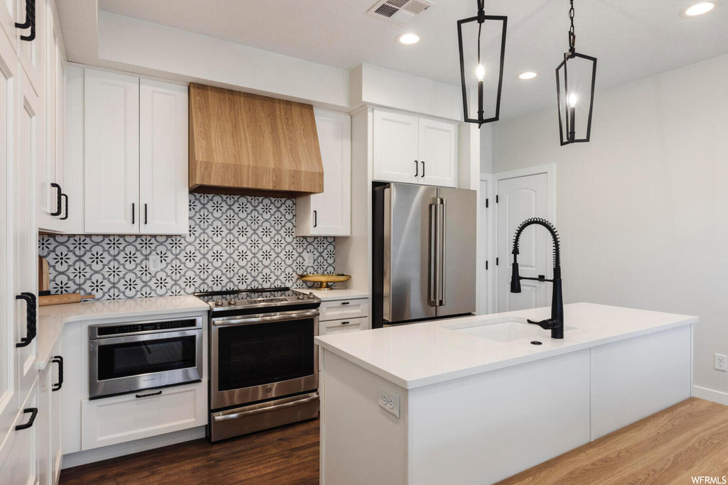 Kitchen with custom exhaust hood, white cabinets, appliances with stainless steel finishes, and hardwood / wood-style flooring