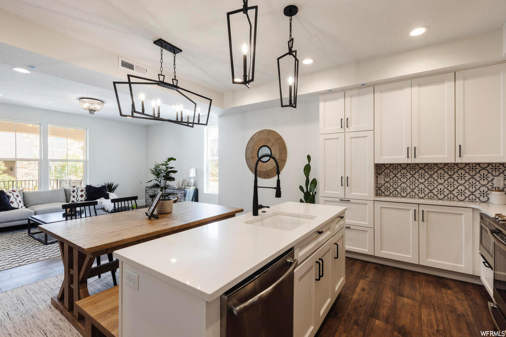 Kitchen with a chandelier, a kitchen island with sink, stainless steel dishwasher, white cabinets, and decorative light fixtures