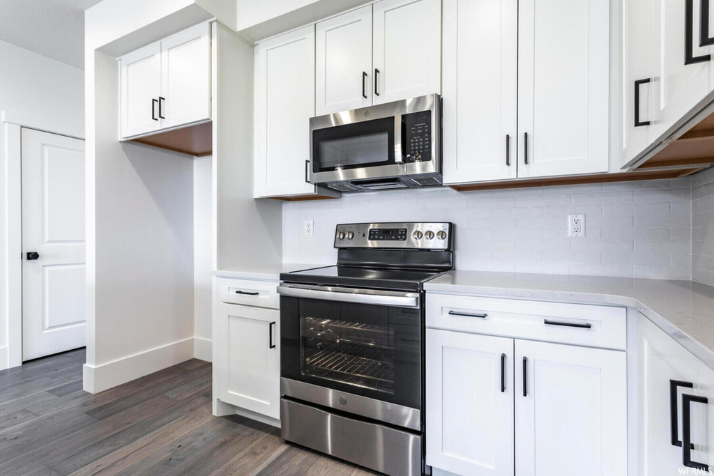 Kitchen featuring tasteful backsplash, dark wood-type flooring, stainless steel appliances, and white cabinetry