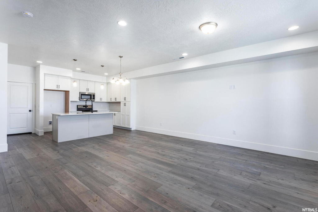 Kitchen featuring an island with sink, stainless steel appliances, white cabinets, decorative light fixtures, and dark hardwood / wood-style floors