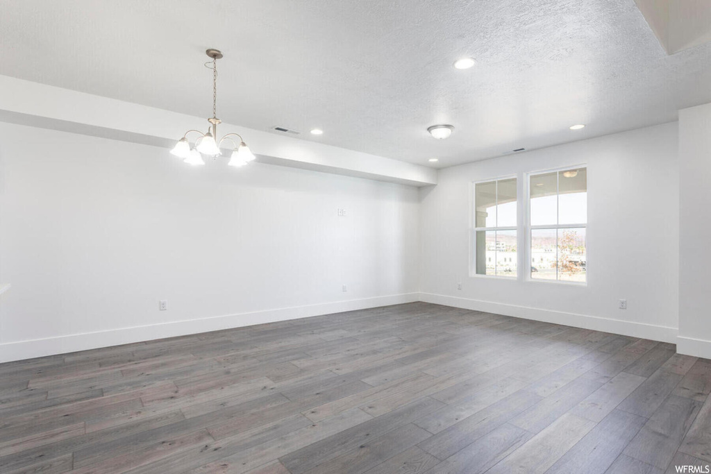 Empty room with dark wood-type flooring, a textured ceiling, and a notable chandelier