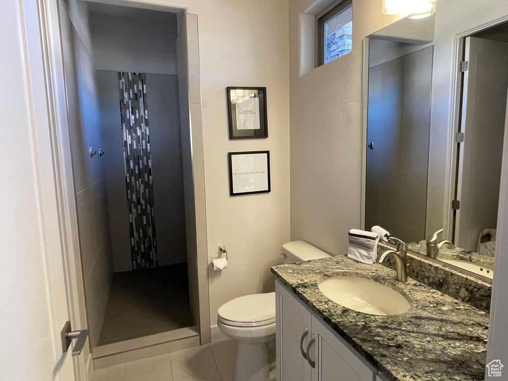 Bathroom featuring vanity with extensive cabinet space, toilet, a tile shower, and tile flooring
